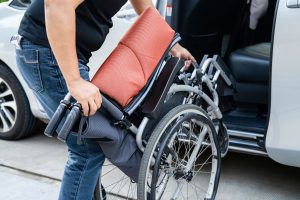 Asian woman folding and lift up wheelchair into her car.