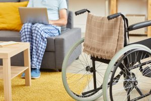 Image of wheelchair are in the room with senior man using laptop on the sofa in the background